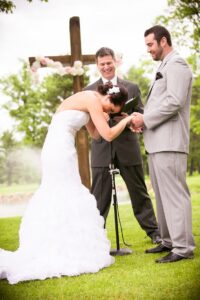 Bride in white dress holding groom's hand, officiant stands between them
