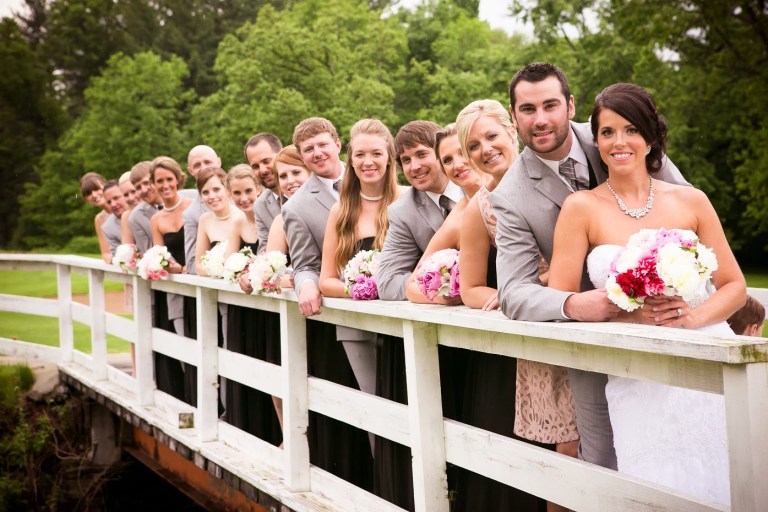 Bridal party in formal attire lined up on a wooden bridge
