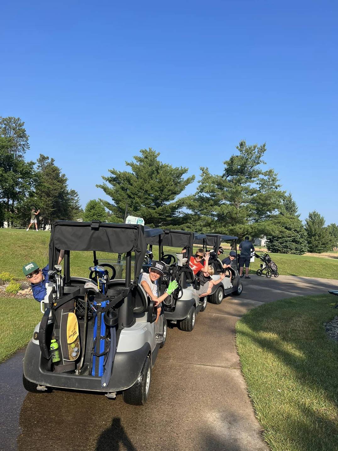 Kids sitting in three golf carts waving at the camera