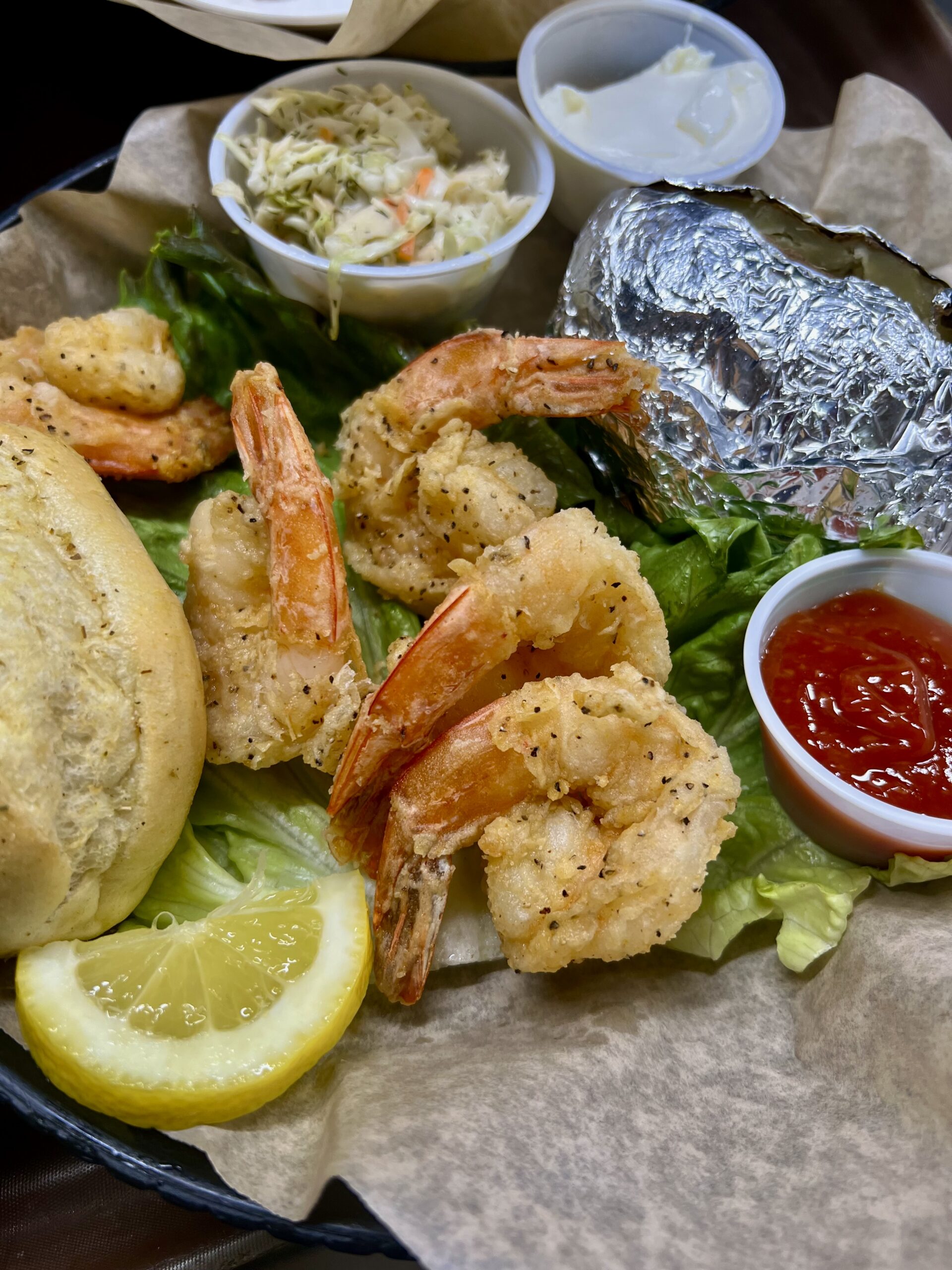 Jumbo breaded shrimp on lettuce with a bread roll and cup of sauce