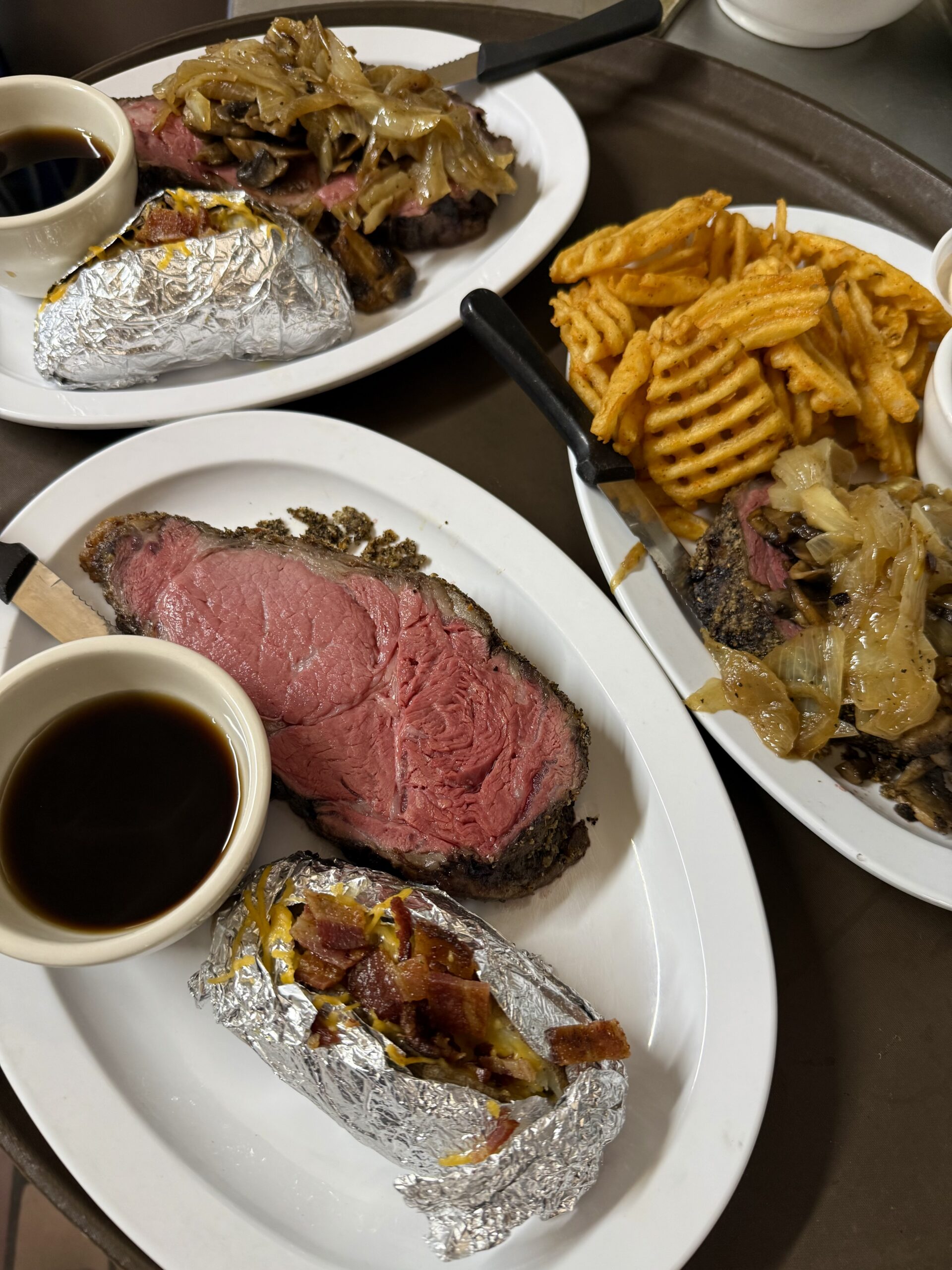 Three plates of steak with sides of fries and bacon bits