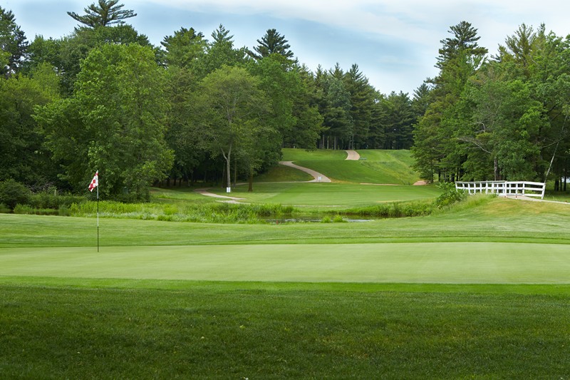 Putting green with a flagstick and bridge leading to a path