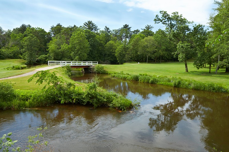 Scenic view of the golf course with a bridge over a creek surrounded by trees