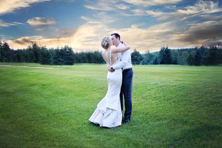 Bride and groom embracing, sharing a kiss on a vast green field