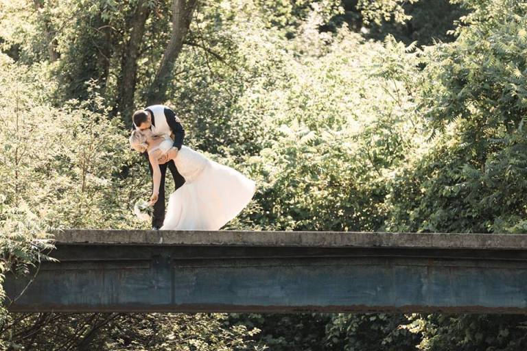 Groom dipping the bride on a bridge surrounded by greenery
