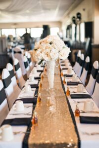 Elegant wedding table setting with gold runner, tall vase of white roses, and neatly arranged place settings