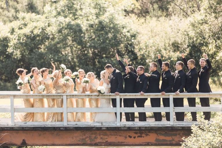 Bridal party standing on a bridge cheering as the bride and groom kiss