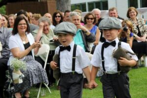 Two young boys in matching caps, suspenders, and bow ties walking hand-in-hand down the aisle