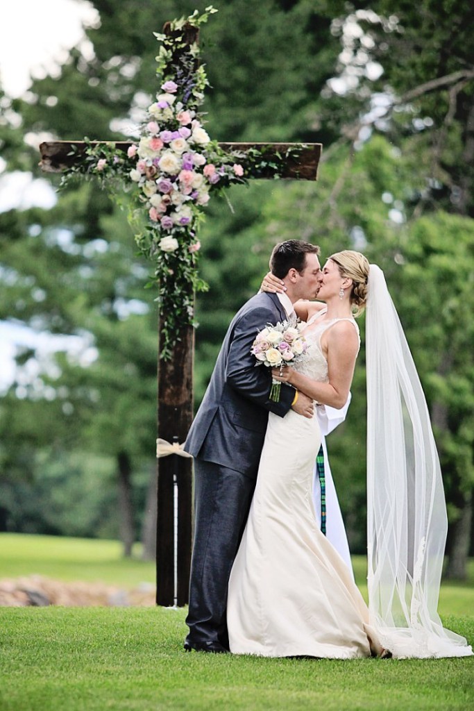 Bride and groom kissing in front of a large wooden cross decorated with flowers