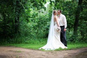 Bride in a white gown and veil standing beside the groom kissing her cheek