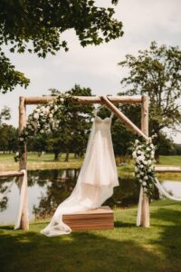 Wedding dress hanging on a wooden arch adorned with flowers