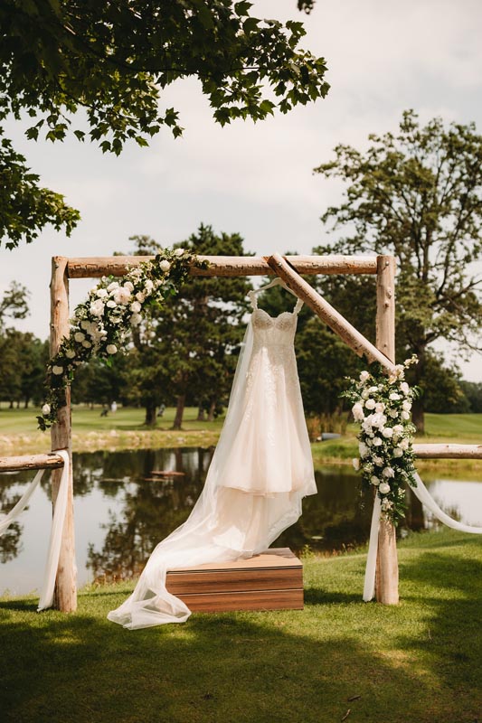 Wedding dress hanging on a wooden arch adorned with flowers