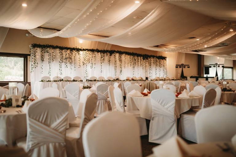 Elegant wedding reception hall with draped ceilings, decorated tables, and chairs