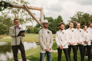 Groom in a beige jacket and cowboy hat standing with groomsmen at an outdoor ceremony