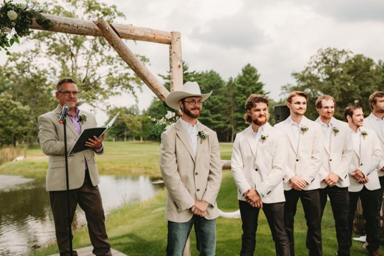 Groom in a beige jacket and cowboy hat standing with groomsmen at an outdoor ceremony