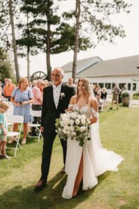 Bride in a white dress holding a large bouquet while walking down the aisle with her father