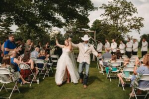 Bride and groom walking down the aisle outdoors while guests cheer