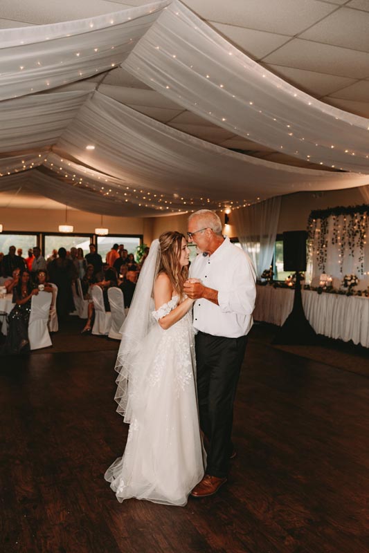 Bride in a white dress and veil dancing with an older man